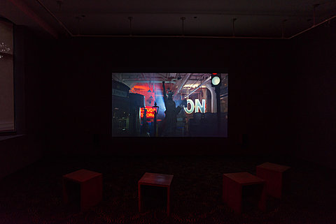 Three small benches sit in a dark room in front of a projection.