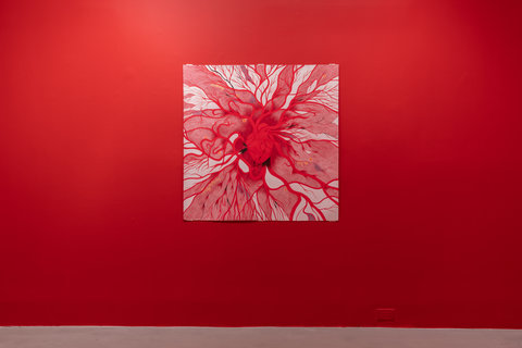 Installation view of the exhibition featuring one large drawing of an anatomical heart. The drawing sits in the center of a bright red wall. Red lines like veins are protruding and emerging from the anatomical heart in all directions against a white background. 