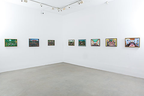 The corner of a gallery room with eight color paintings hanging on the walls.