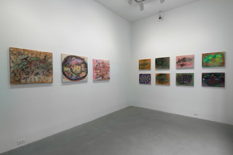 Installation image of the exhibition featuring three paintings hung against a white wall on the left side of the room. On the right side of the room, two rows of four paintings are hung evenly apart. 