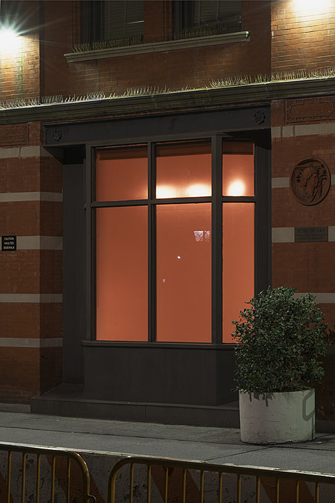 An exterior view of a building at dusk with glowing yellow light visible through the window.