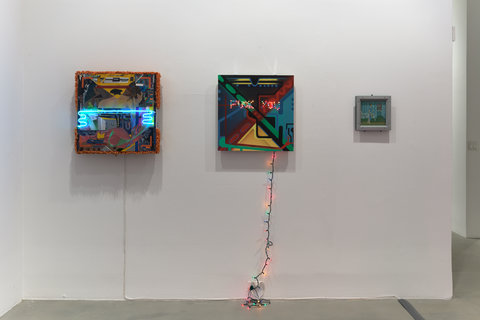 Installation view of three works hung against a white wall in the exhibition. The first work consists of a darker color pallet with a blue neon stripe through the center. The middle work consists of multiple colors and multicolored christmas lights which travel down the painting, down the wall and plug into an outlet near the floor. The last work is much smaller compared to the rest and consists of blue and green abstraction.  