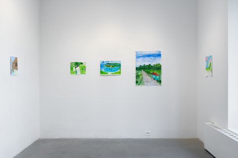 Installation view of three walls. On the left wall there is an drawing of a brown house, with a black window. In front of the house is a white picket fence with grass. A blue sky sits above the house and the background of the image. In the middle wall, there are three drawings in a row. On the left, there is a drawing of what looks like a figure hiding under a white sheet on a grassy field. In the middle image, there is a landscape drawing of green, hilly islands, bright blue pools of water and light yellow sandy beaches. On the right image, the last image in the row on this wall, there is a grey road descending into the background. On the right of the road is a small turquoise house with a red, shingle roof. The road leads into the distance of green pointed mountains and ombre blue skies. On the right hand wall, there is a drawing of pink flowers with green leaves and stem. The flowers are in front of a blue background. Next to this image, light pours in from the right side window.  