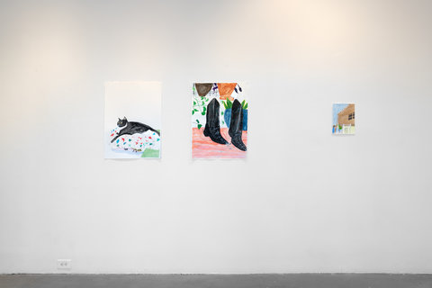 Installation view of the exhibition featuring a white wall with three drawings hung in a row. The drawings are done a bit abstractly, but still easily representational of figures and objects. The first drawing is a black and white cat sitting upon a blanket which is dotted in red, blue, and green shapes. The second picture, in the middle, is of a pair of black Cowboy boots. They are standing on a reddish-orange floor with sketches of potted plants in the background. On the right, is the last drawing of the outside view of a brown house. The house has one black window crossed perpendicularly with brown cross bars. The sky above the house is bright blue and a white fence sits in the foreground. 