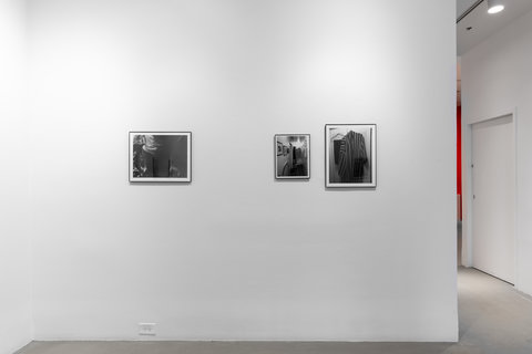 Installation view of three works in the exhibition. On the left side there is a black and white photograph and on the right side there are two black and white photographs closer together. The furthest left photograph is a bit bigger than the center photograph. The images in the photos are difficult to make out due to the glare of the lights in the glass frames. 