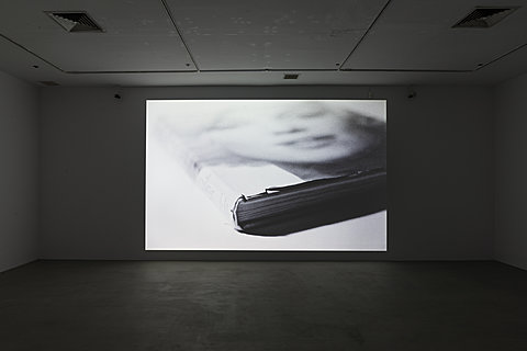 A large floor-to-ceiling projection of a face on a book cover. The projected image is stretched horizontally.