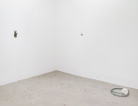 Installation view featuring two walls and the floor of the exhibition. On the left wall, a very small image of an abstract, droid like figure is hung on the wall. An image on the right wall is hard to make out, and sort of blends into the wall. Pennies are scattered across the cement floor. On the right side of the floor, a plastic opaque white funnel sits in two glass rimmed discs. 