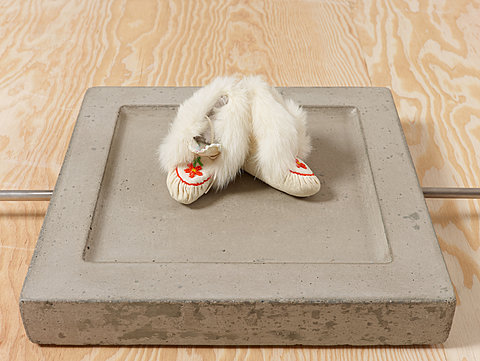 A pair of white moccasins rest on a concrete plinth.