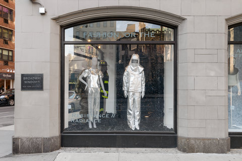 Image of two mannequins in the exhibition. The left mannequin wears a silver shirt and silver pants. The mannequin on the right wears a full silver space-like costume with a silver fabric helmet. 