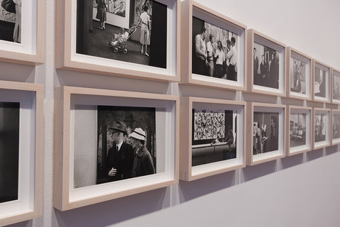 Close-up image of several black and white photographs hung in two rows in small white frames. 