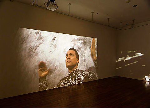 A large projection on a gallery wall shows a person with their eyes closed.