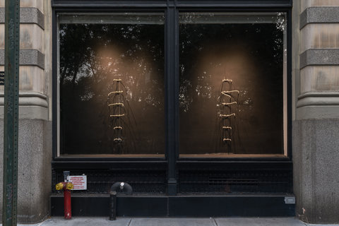 Close up view of a light colored building with a large dark window. Inside the window on the left and right sides are 6 short horizontal warm toned neon lights.