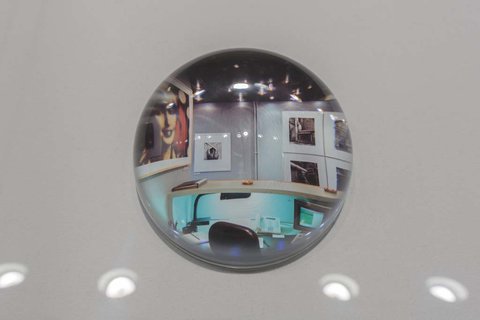 Close-up image of a glass orb in the exhibition atop a white pedestal. The glass orb's convex shape allows for the image underneath to show through in a bit of a distorted way. 