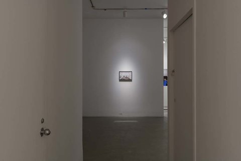 Installation view of the exhibition featuring one art work spotlit on the back white wall. The artwork is illegible from this camera angle. 