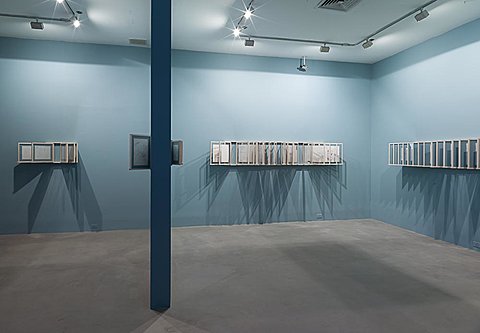 Two adjacent rooms in an art gallery have drawings displayed against blue gallery walls.