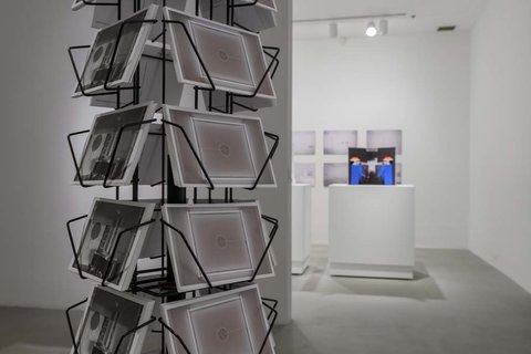 Close-up image of the postcard carousel with the same image in each slot. The carousel is close-up in the foreground of the image on the left. On the right, in the background a blurred white pedestal with a monitor. 