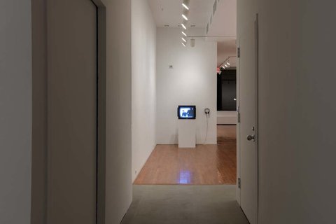 Installation image of a white pedestal featuring a television monitor sitting on top of it. 