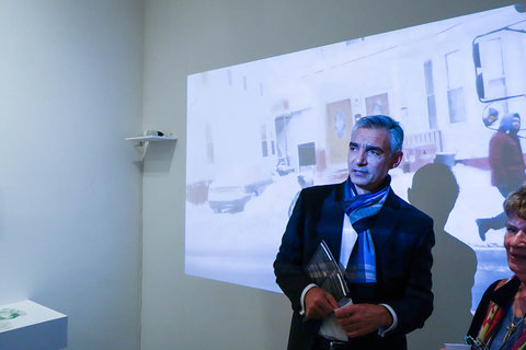 View of a visitor in the gallery standing in front of a projection against a white wall in the exhibition. 