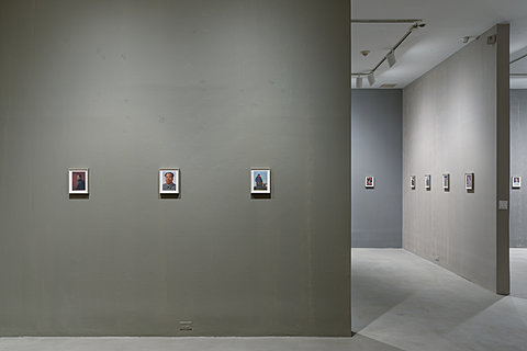 A gallery with gray walls and numerous small pictures of Chairman Mao mounted on the wall.